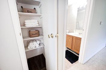 A white closet with shelves and a door leading to a bathroom.